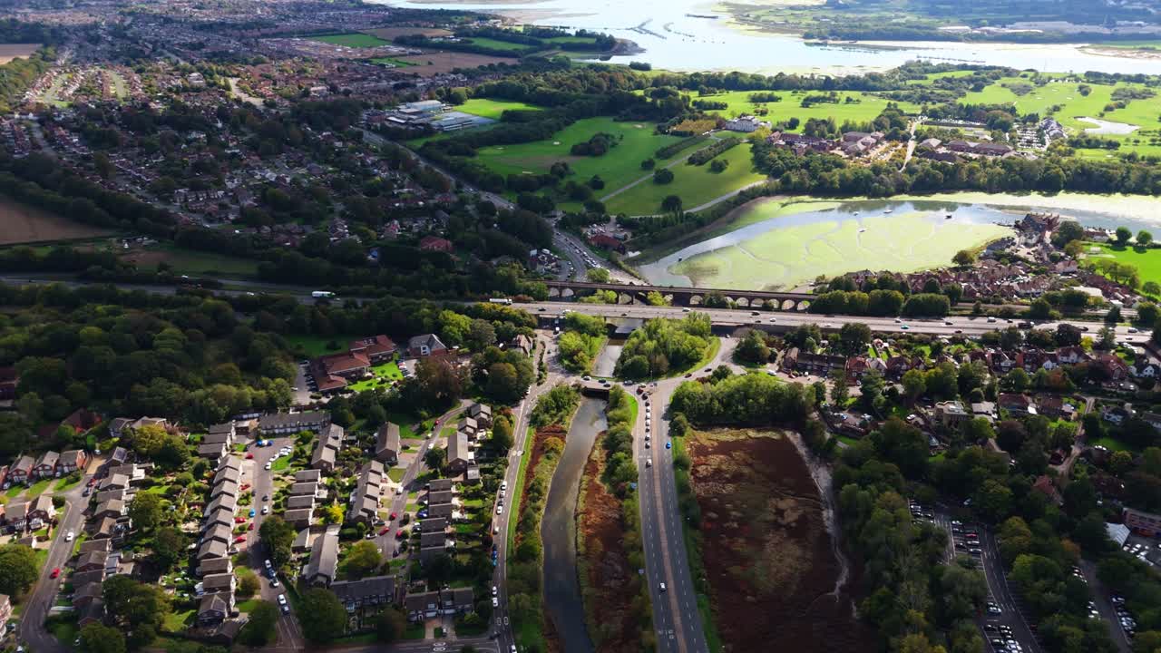Aerial drone pans right over Fareham roundabout with river and water, capturing fields, roads, cars, and autumn nature glowing warmly in golden sunset light across the scenic English countryside