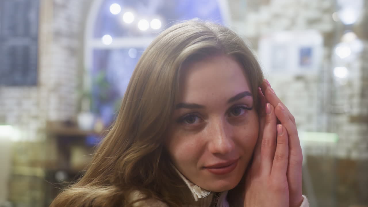 Close-up of beautiful girl resting face on hands in cozy cafe, peaceful moment captured, relaxed and serene expression, warm ambiance creating tranquil and comforting atmosphere