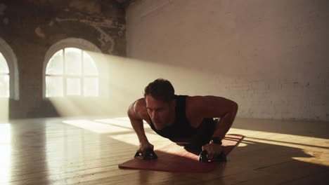 Close-up-shot-of-a-man-in-black-sportswear-summer-uniform-doing-push-ups-using-special-hand-rests-on-the-Red-Mat-in-the-Sunny