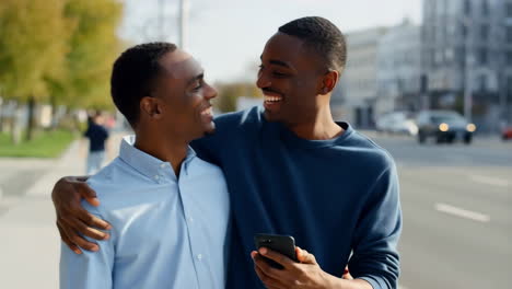 two young men smiling and looking at a smartphone outdoors