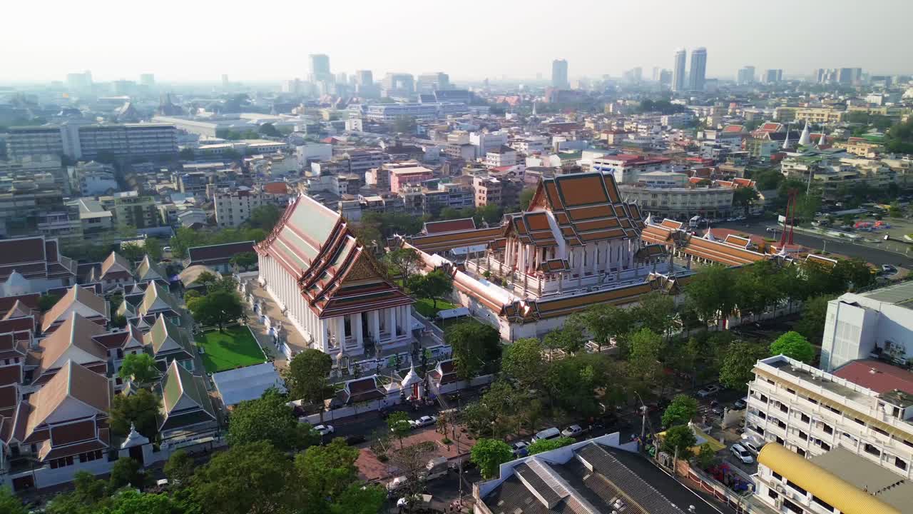 Aerial orbit clockwise of Wat Suthat temple in Bangkok, red roof, golden decorations, and spacious temple grounds