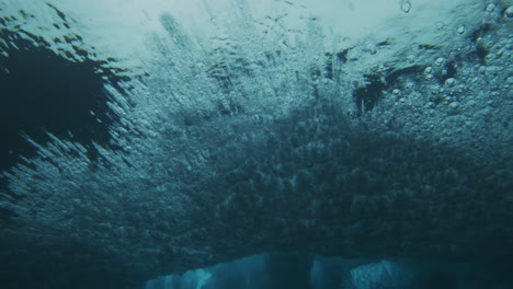 Turquoise-underwater-angle-texture-of-crashing-wave-spreading-bubbles-across-surface-and-cloud-of-water