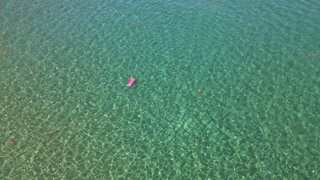 Tourist With Airbed Swimming In The Middle Of The Tropical Crystal Clear Sea During Summer In Sardinia, Italy - aerial, top down