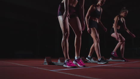 female runners at athletics track crouching at the starting blocks before a race. in slow motion.