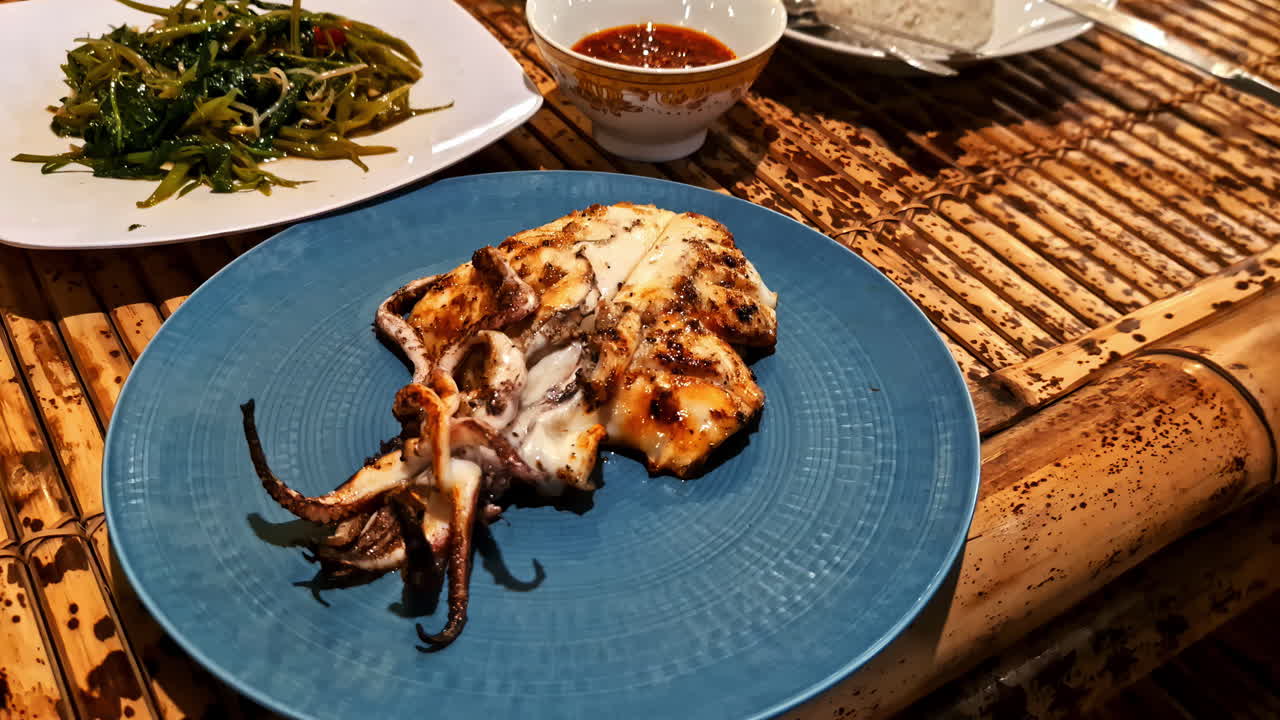 Indonesian seafood meal: grilled squid, rice and vegetables on a bamboo table