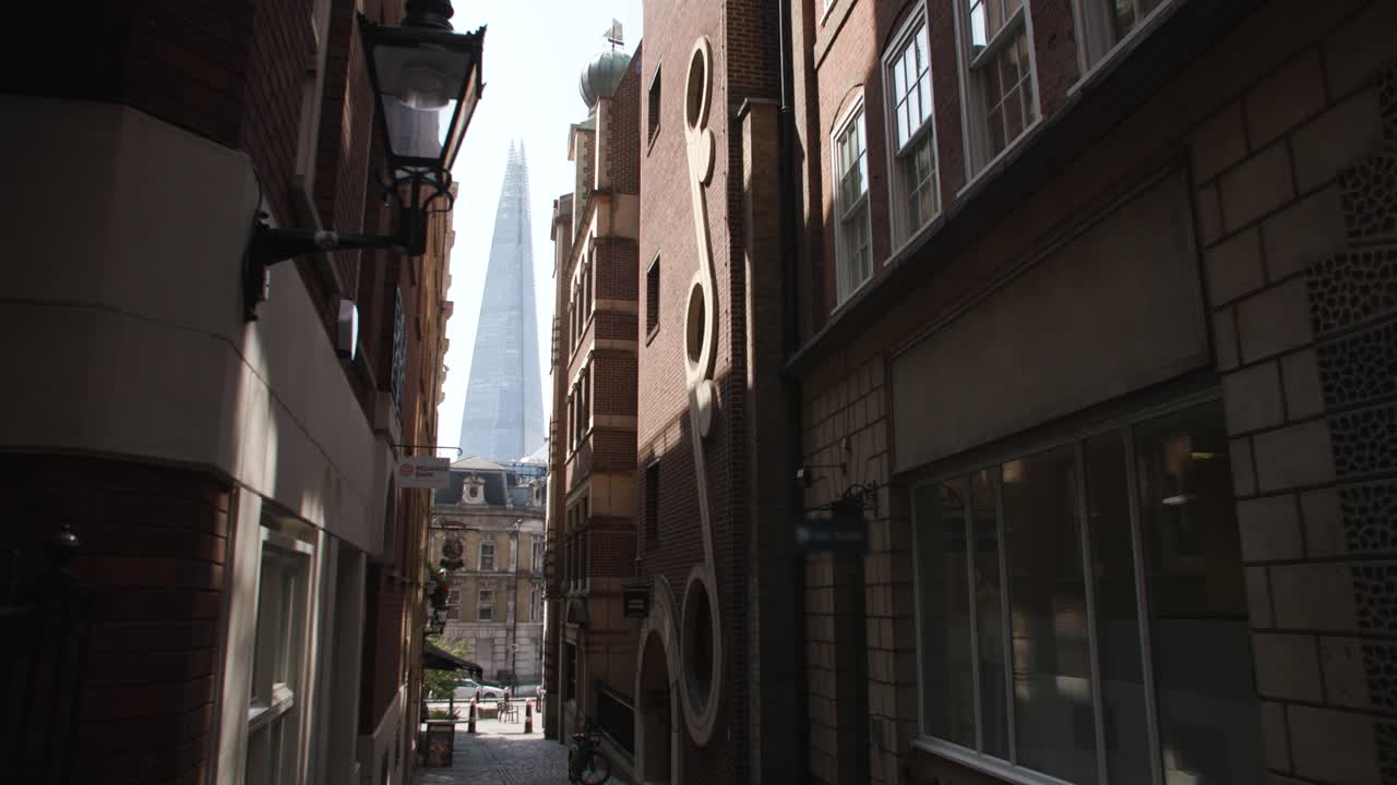 The Shard, London stands tall, framed between row of buildings on small cobblestone street