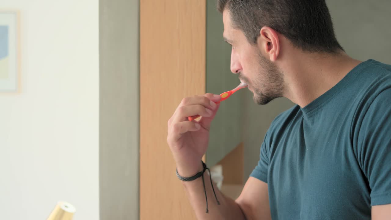 Man raising orange toothbrush to mouth, brushing teeth methodically at wash area for oral care