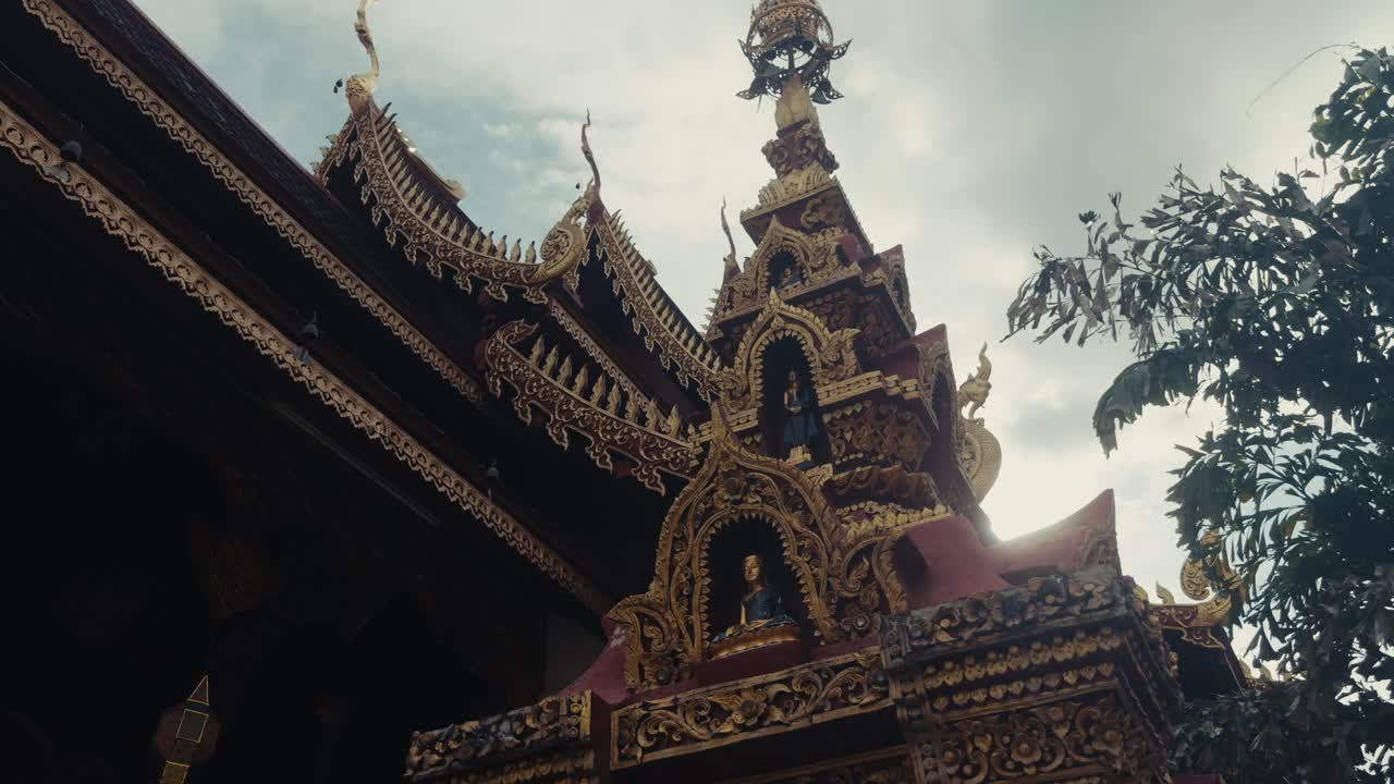 Guglia di un tempio tailandese finemente decorata con statue dorate di Buddha e intagli dettagliati sotto un cielo nuvoloso