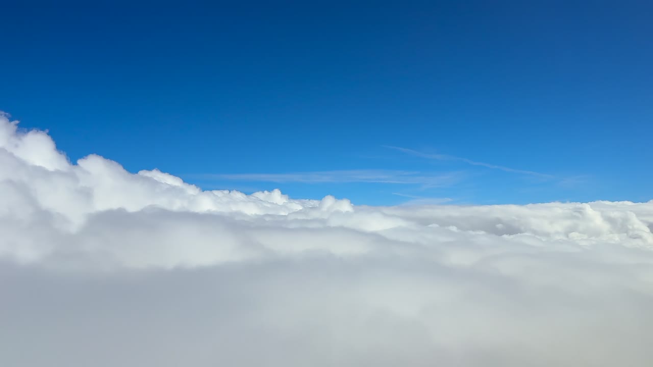 A pilot’s eye view from a jet cockpit, flying at supersonic speed over and into an endless sea of white clouds, under a deep blue sky