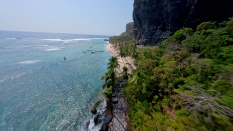 Dynamic-drone-flight-along-shoreline-with-tourist-on-sandy-beach-and-palm-trees-during-sunlight---PLAYA-FRONTON,-Dominican-Republic