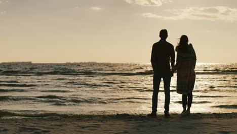 couple in love looking at the sunset over the sea holding hands cool day the wind is blowing back vi