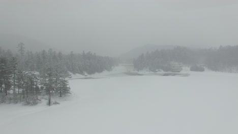 dron volando sobre un lago cubierto de hielo blanco durante una tormenta de nieve hacia el bosque