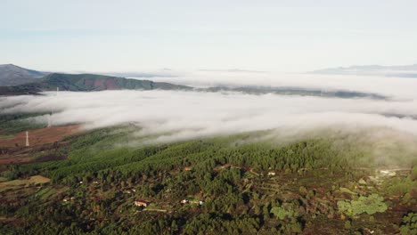 Drone-shot-of-sun-drenched-hilly-landscape-with-mountains,-fields-and-trees