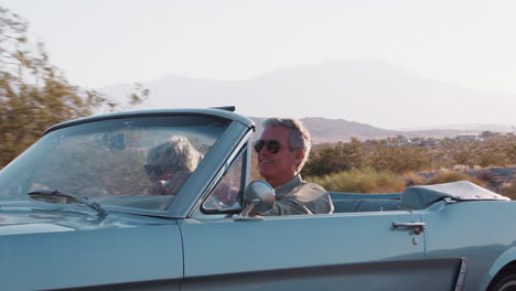 pareja blanca senior conduciendo un descapotable clásico en la autopista