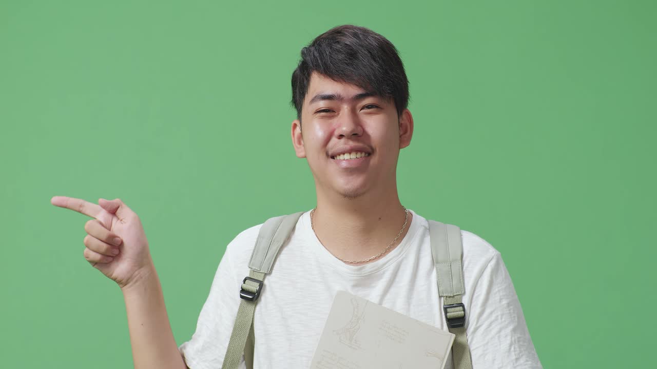 녹색 스크린 스튜디오에서 책을 들고 손가락을 는 아시아 남성 학생의 클로즈업