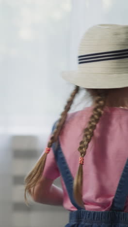 ein hübsches kleines mädchen mit strohhut steckt lieblingsspielzeug in einen koffer mit der mutter im wohnzimmer in nahaufnahme. tochter mit blonden zöpfen bereitet gepäck für die reise vor