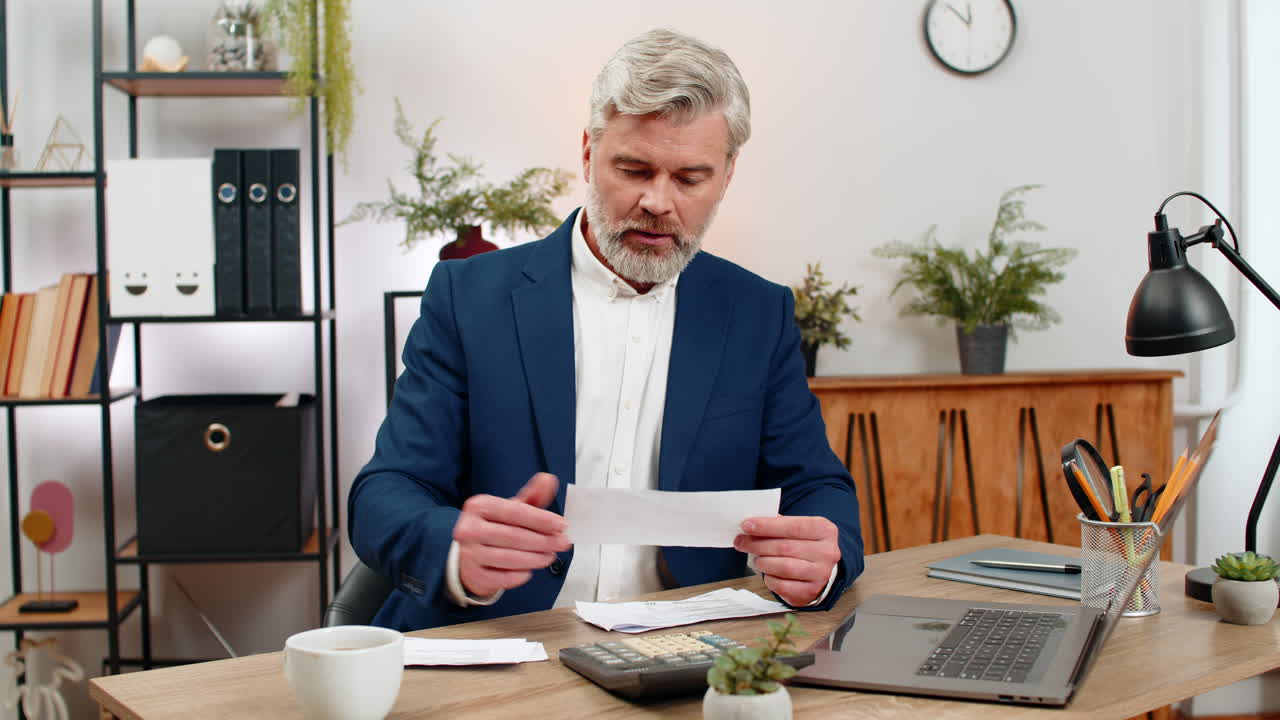 Middleaged businessman reviews budget with laptop calculator receipts stack frowning over balance