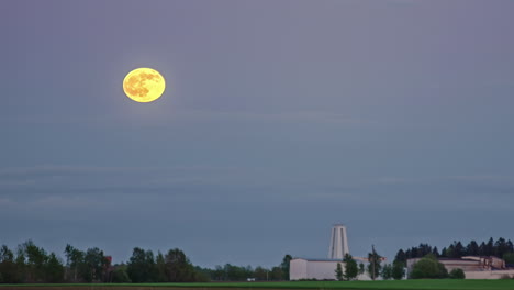 vídeo timelapse de la luna saliendo sobre un cielo azul en un paisaje rural con vistas a un edificio blanco a distancia
