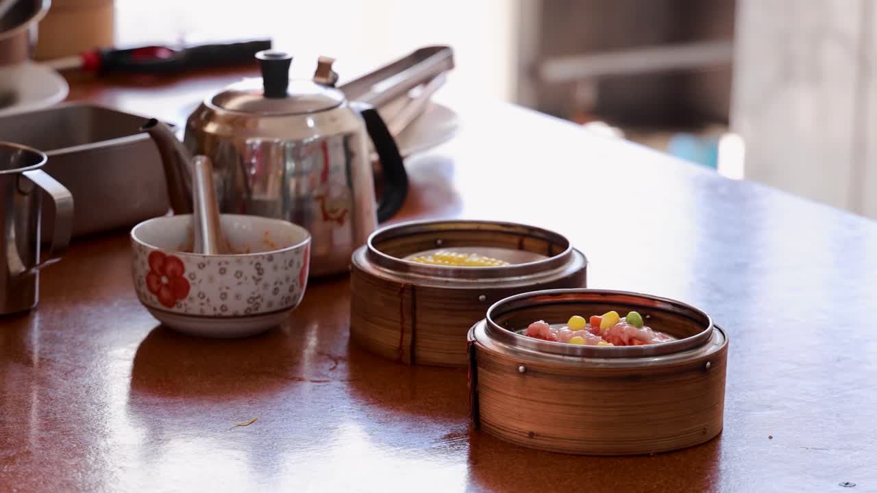 A person serves dim sum in bamboo steamers on a wooden table in a Phuket restaurant, with natural lighting