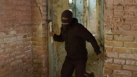 man in a balaclava and holding an ax running in a ruined building