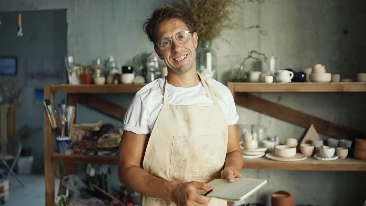 retrato de un joven alfarero feliz posando en su estudio de cerámica