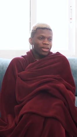 young man resting on a couch wrapped in a blanket