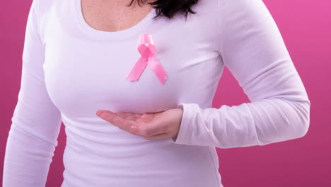 video of midsection of caucasian woman wearing pink cancer awareness ribbon, with pink background