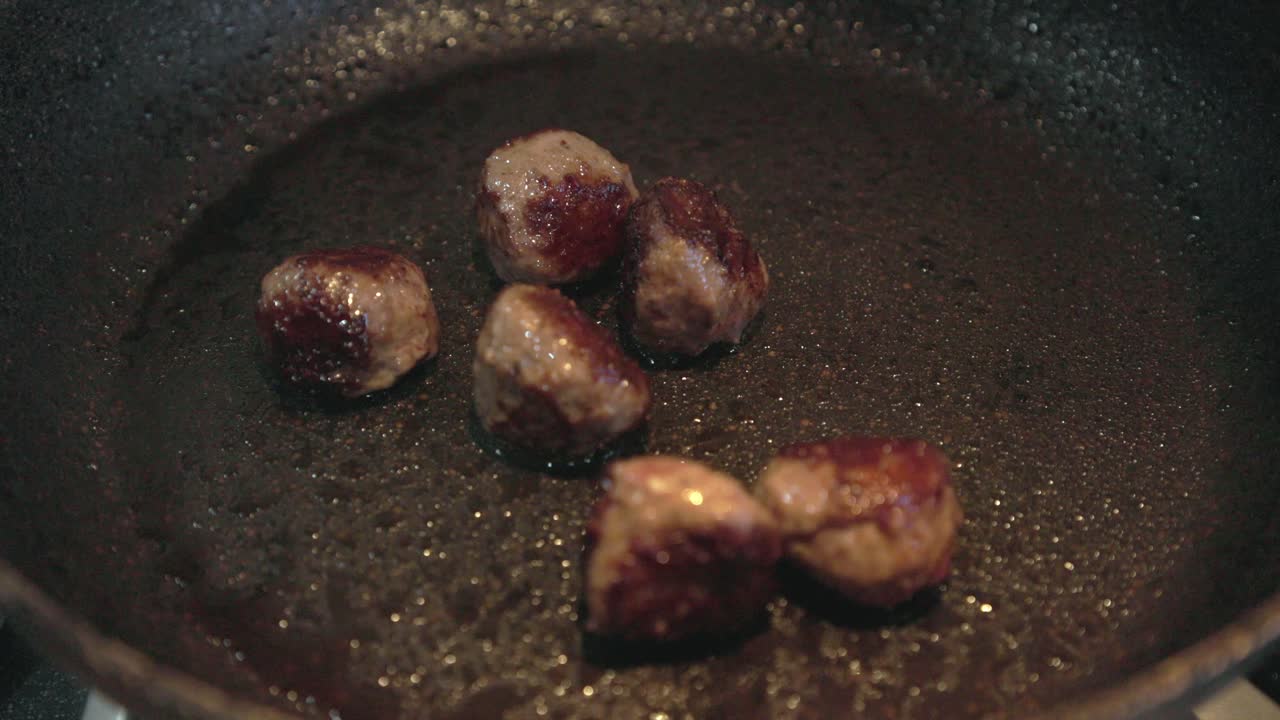 フライパンで焼かれ、焼き色がつくミートボールのスローモーション映像。