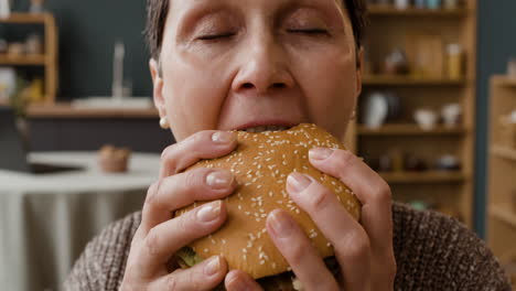 close-up of a mature woman eating a hamburger at home