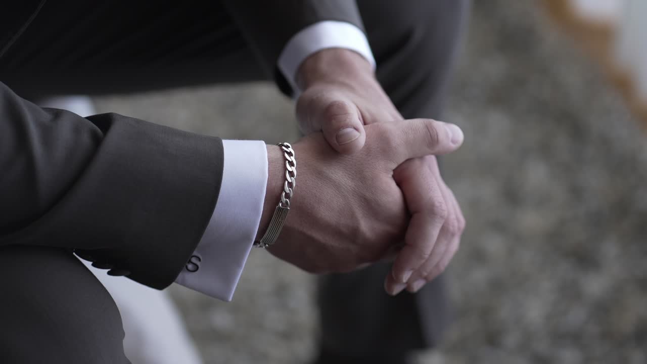 primer plano de las manos de un hombre unidas, con un traje y un brazalete de plata