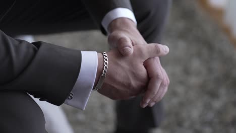 primer plano de las manos de un hombre unidas, con un traje y un brazalete de plata