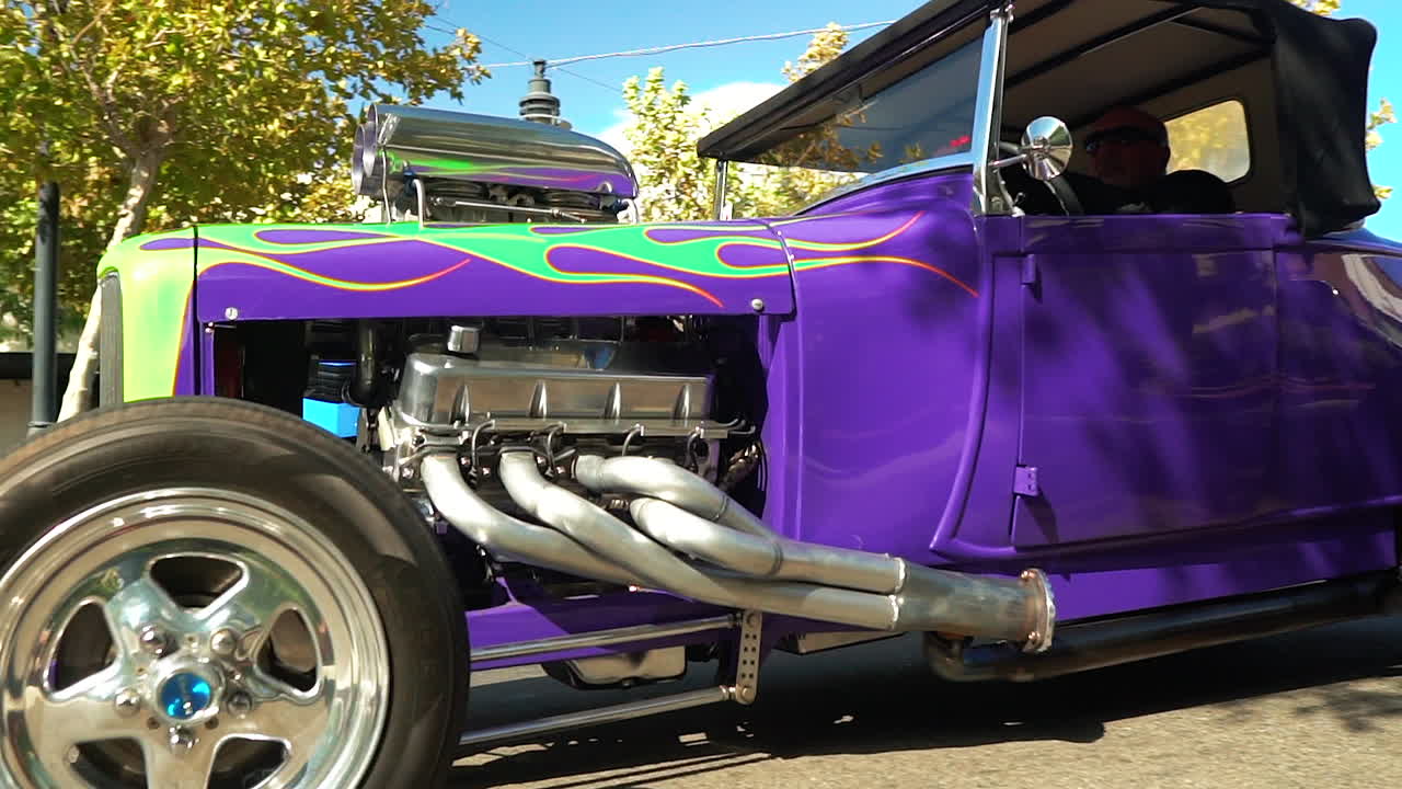 Purple hot rod with green flames paint job drives past, slow-mo