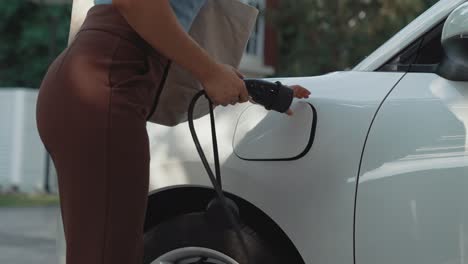 Progressive-woman-installing-plug-from-home-charging-station-to-electric-vehicle