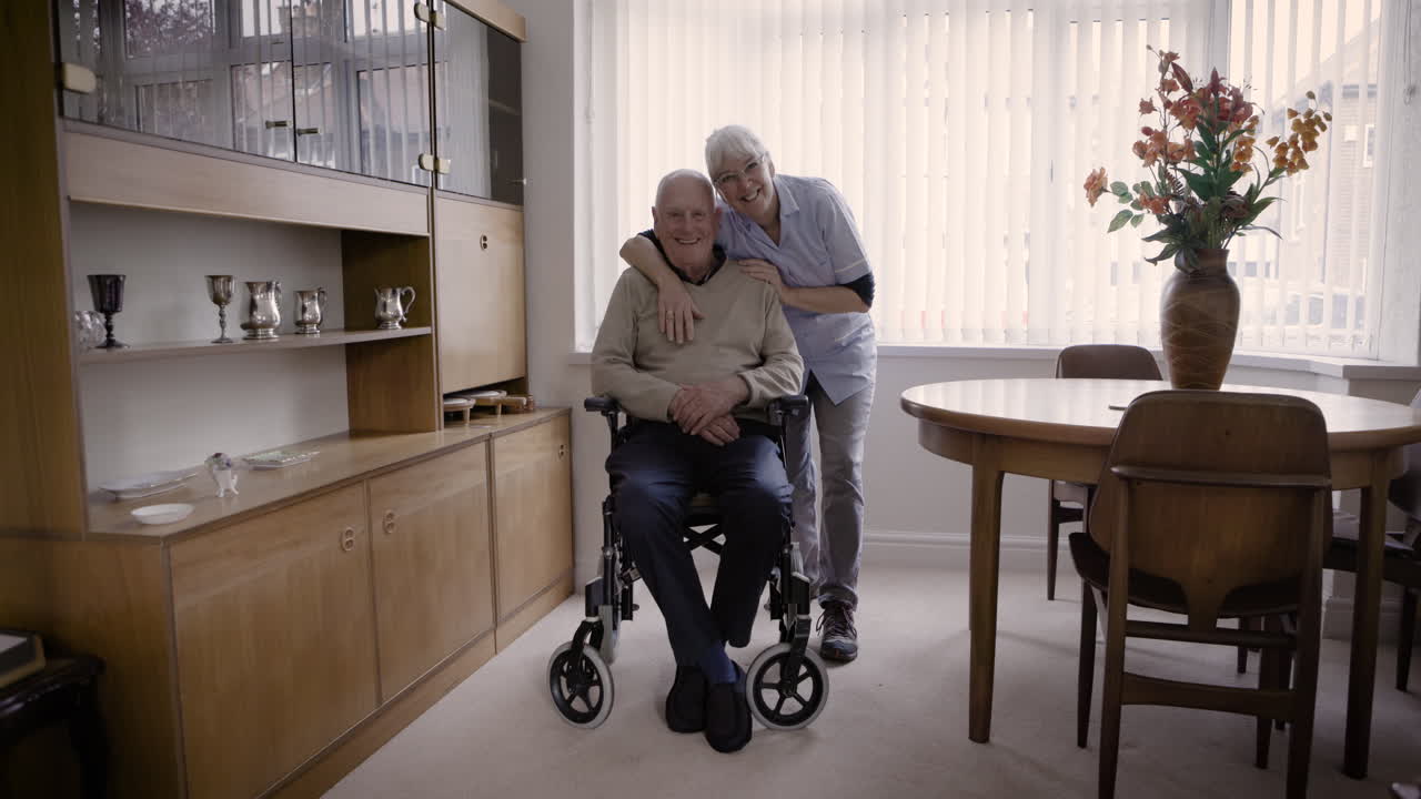 Elderly man in wheelchair with caregiver in living room