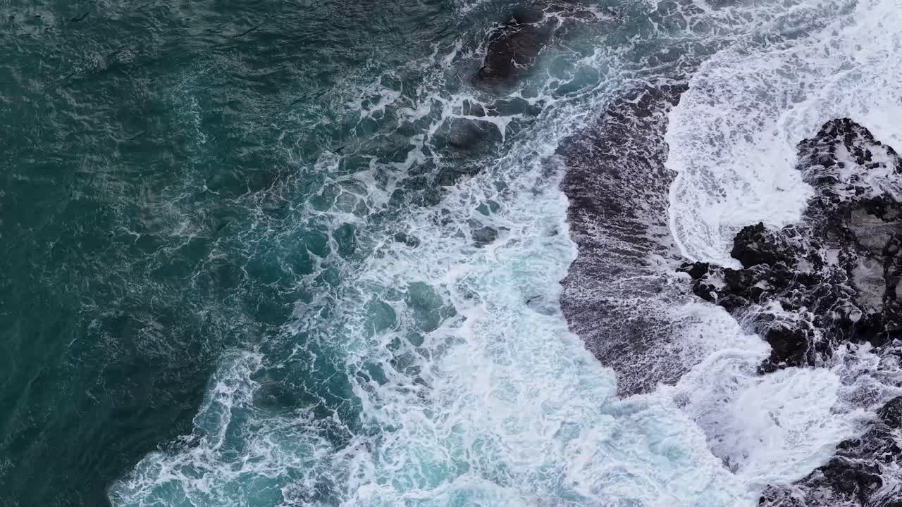 Drone riprende onde turchesi che si infrangono sulle rocce scure a Cape Schanck, luce naturale, movimento fluido
