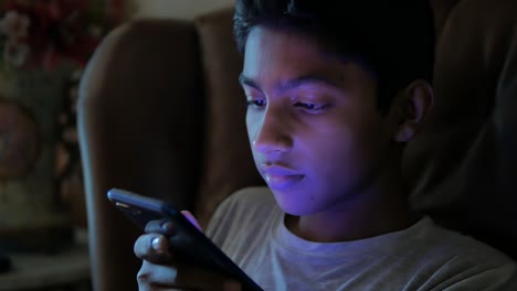 teenage boy sitting on sofa using smart phone at night