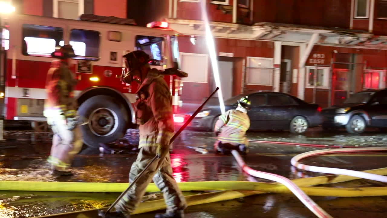 A Fireman Carries Equipment Across a Street with Firetrucks and Flashing Lights in the Background