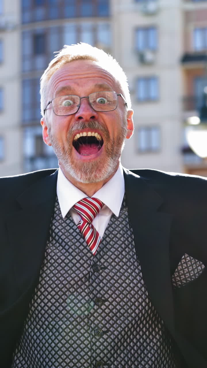 Senior businessman in glasses and suit talks happily on the city background. Enthusiastic middle aged man talking and showing happy gesture with his arms. Vertical video