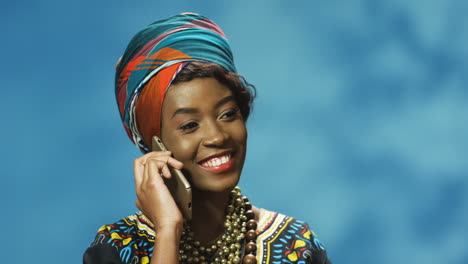 visão aproximada de uma jovem afro-americana em turbante e roupas tradicionais falando ao telefone