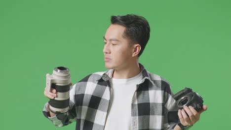 close up of asian photographer changing lens of camera before using it taking pictures while standing on green screen background in the studio