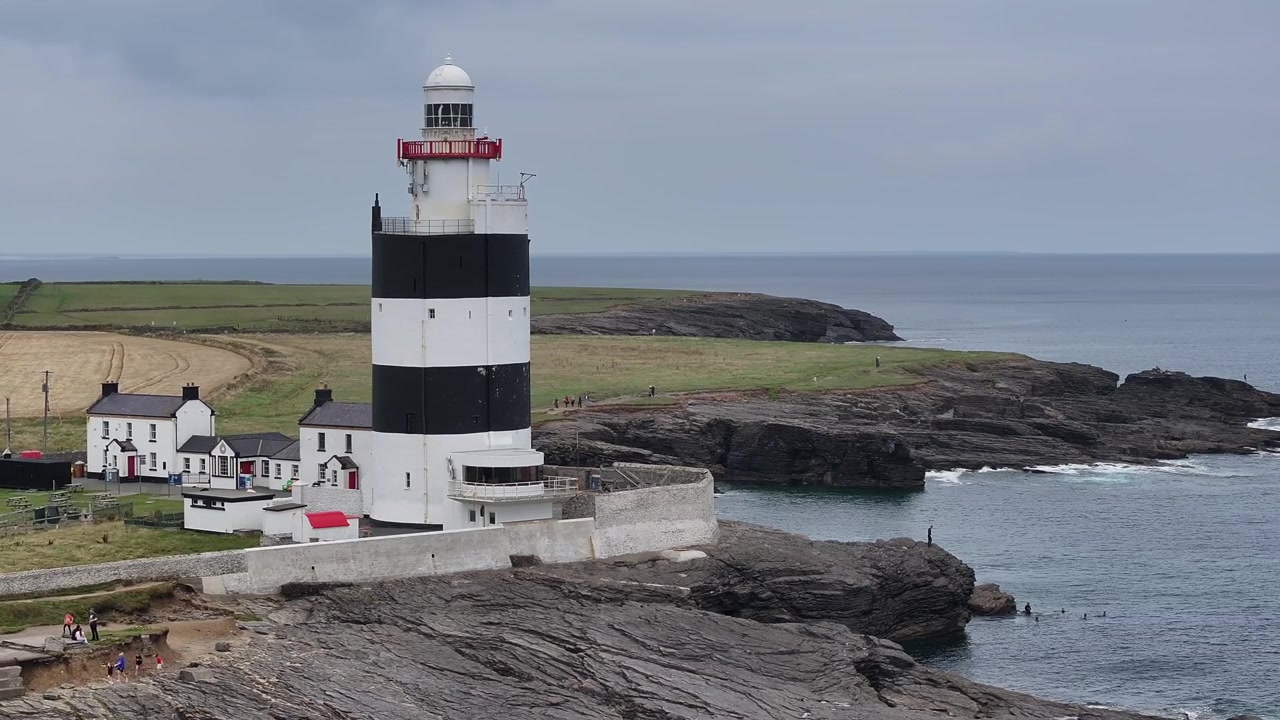 Luftfoto af det ikoniske sort- og hvidstribede Hook Fyr i Wexford, Irland. Dette historiske vartegn står på en barsk klippekyst under en stemningsfuld himmel