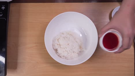 placing boiled rice into white bowl and mixing it with red sauce and oil