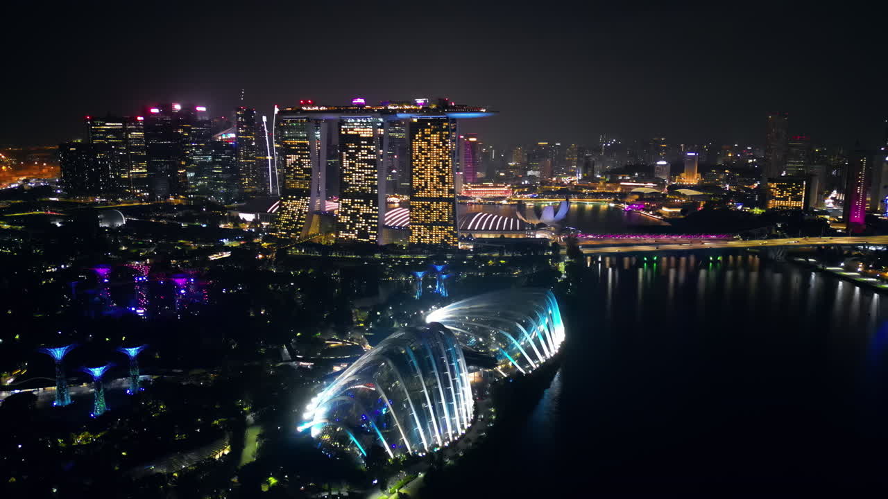 Marina Bay Sands'i, Singapore Flyer Gözlem Tekerleğini ve Aydınlatılmış Sahil Şeridini Gösteren Singapur Marina Koyu'nun Gece Hava Drone Görüntüsü