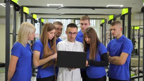 a doctor analyzes data in a gym showcasing teamwork in fitness in a gym individuals gather around a doctor analyzing data on a laptop the collaborative atmosphere highlights teamwork and innovation in fitness