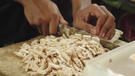 hands cutting tofu into thin slices with sharp knife, close up