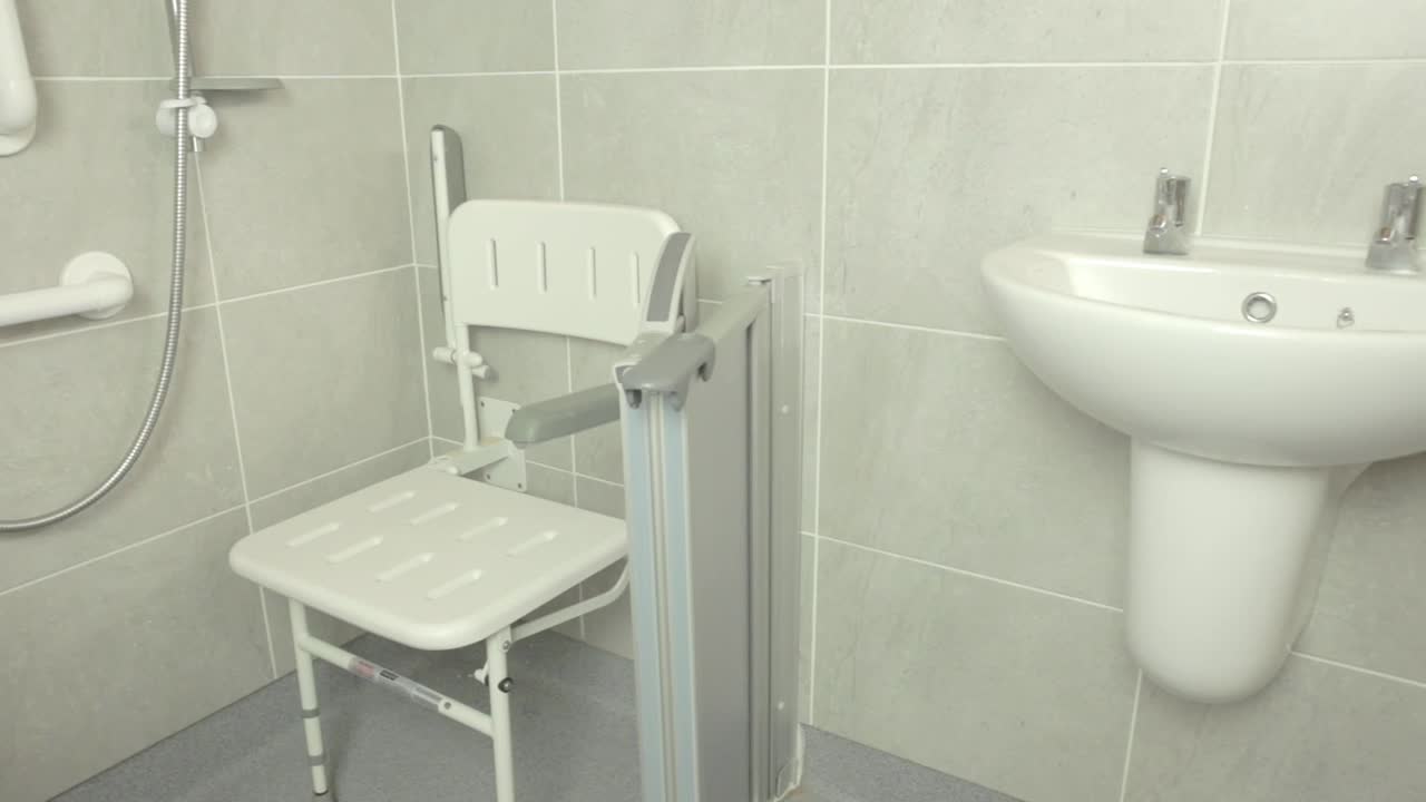 Pan shot of disabled adjustable shower seat in wet area bathroom with sink and against tiles