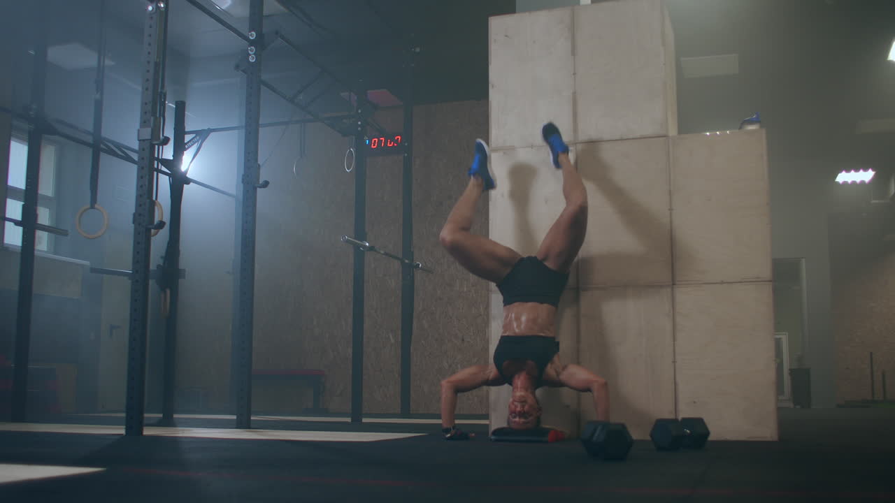 a strong woman performs vertical push-ups standing on her head in the gym. perform push-UPS upside down. push-UPS against the wall upside down