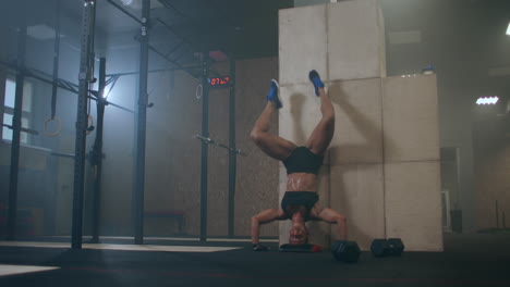 a strong woman performs vertical push-ups standing on her head in the gym. perform push-ups upside down. push-ups against the wall upside down