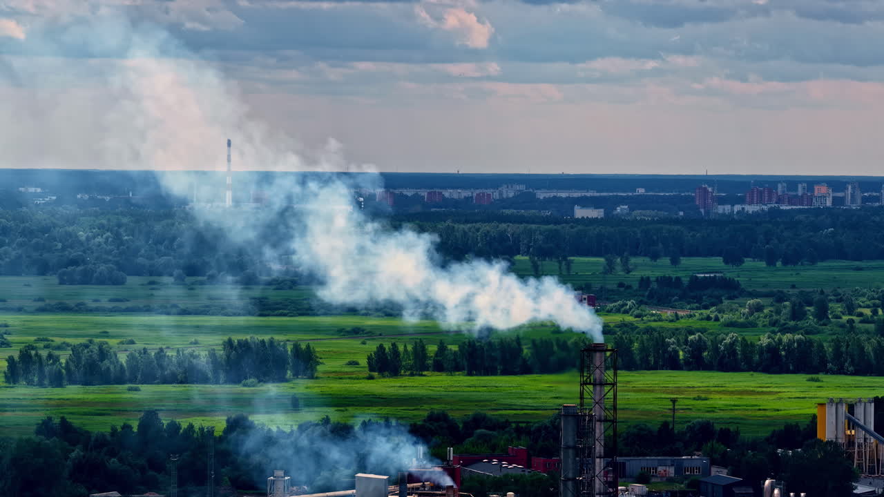 Smoke rises from an industrial chimney against green fields and distant cityscape near Riga. Riga, Latvia