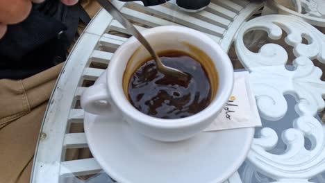 person stirring coffee at outdoor café